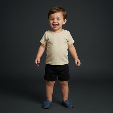 Toddler boy wearing a Palm and Pale cream short-sleeve t-shirt with shoulder snaps and black cotton shorts, available in sizes 0 to 24 months.