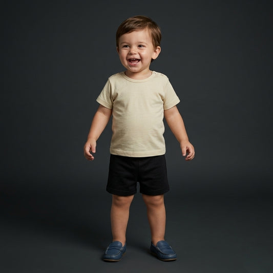 Toddler boy wearing a Palm and Pale cream short-sleeve t-shirt with shoulder snaps and black cotton shorts, available in sizes 0 to 24 months.