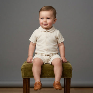 Baby boy wearing a Palm and Pale off-white textured knit short-sleeve romper with Peter Pan collar and button-front detailing, paired with tan loafers.