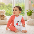 A baby sitting on a white carpet in a bright room, wearing a two-tone long-sleeve romper with coral pink and white panels and a cartoon elephant graphic on the front.