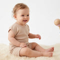 miling baby wearing beige drop-shoulder t-shirt and matching shorts, sitting on soft rug in minimal studio background – summer baby outfit by Palm and Pale