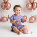 A baby girl is weared a palm and pale purple color today will be a good day print with frill shirt and frill short to repesent the premium quality of coton fabric for summer weather for newborn baby to 5 years baby girl.