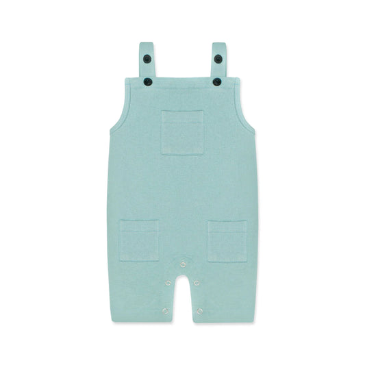 A pastel blue newborn romper with button-on-shoulder straps and front pockets, displayed against a light background with orange and green design elements. The text highlights features like 'Button on Shoulder,' 'Pockets,' and 'New Arrivals.' The brand name 'Palm and Pale' and website 'palmandpale.com' are also visible. The tagline reads 'Sunny styles for little smiles.'