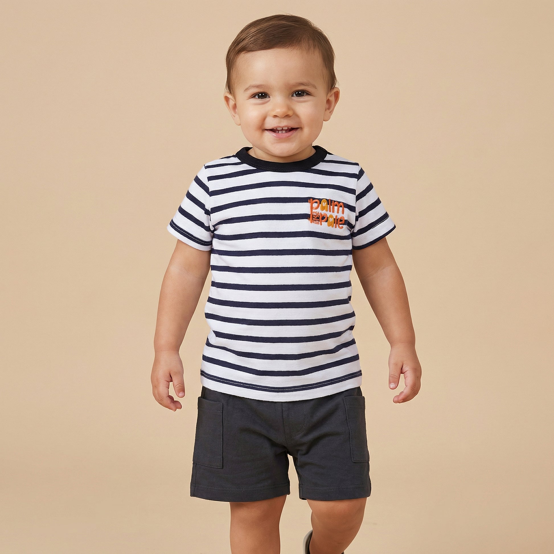 A model of Palm and Pale weared a stripe shirt and balck short by sowing the signature of baby clothing brand palm and pale for 1 year baby to 5 year baby boy in summer cotton pk fabric.