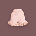 A pair of baby shorts in a soft pastel pink color, displayed against a muted brown background. The shorts are made from ribbed fabric and feature an elastic waistband for comfort. The leg openings are adorned with delicate ruffled hems, adding a cute and stylish touch.