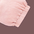 A close-up view of a baby garment in soft pastel pink, showcasing the elastic waistband detail. The fabric has a ribbed texture, and the gathered elastic design ensures a comfortable and snug fit. The muted brown background highlights the fine stitching and gentle stretch of the material.