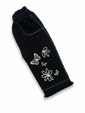 Side view of black girls' denim pants laid flat, showing teal contrast stitching, pocket detail, and butterfly floral print on leg