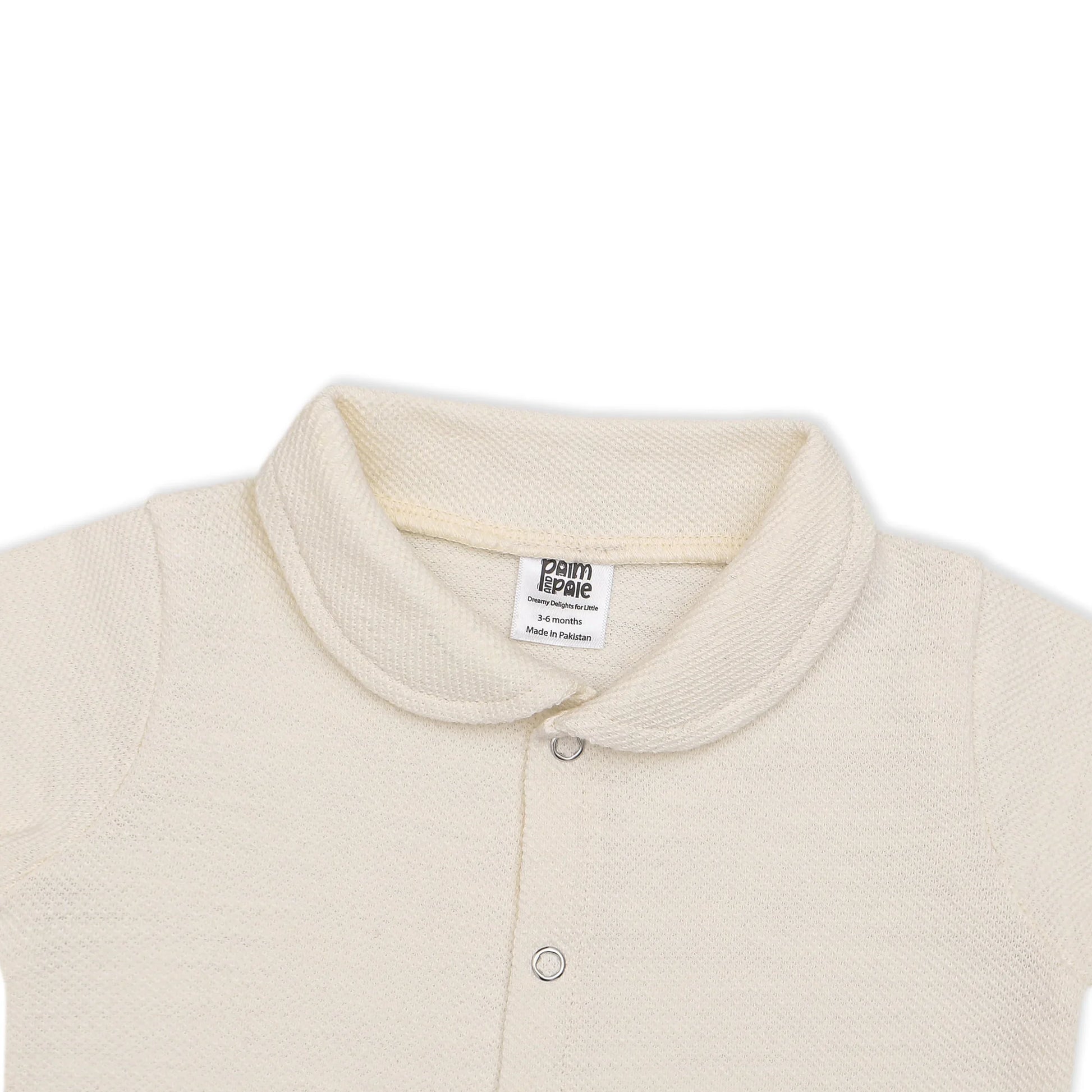 A soft, cream-colored newborn baby romper with a rounded collar, short sleeves, and short legs. The romper features snap buttons down the front for easy dressing. The background includes playful doodles, text highlighting key features like 'Snap Button' and 'Short Sleeves & Legs,' along with 'New Arrivals' branding from Palm and Pale. The tagline at the bottom reads 'Sunny styles for little smiles.'