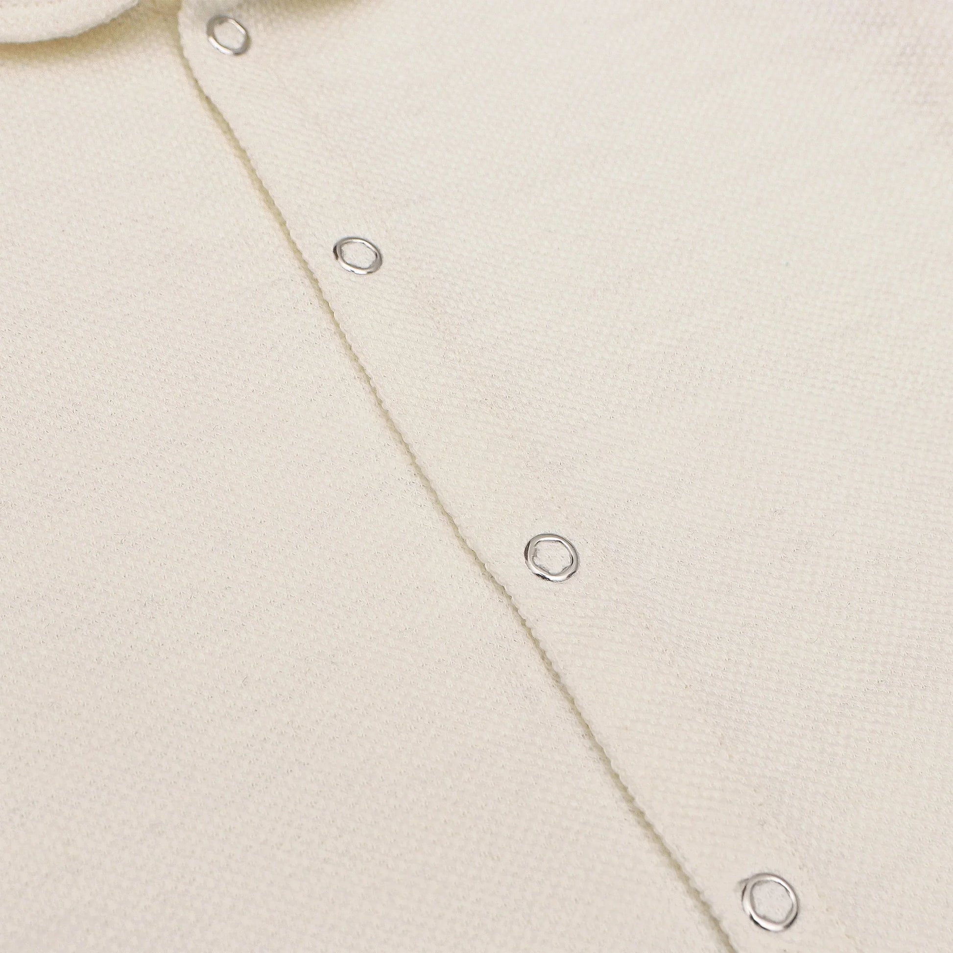 A soft, cream-colored newborn baby romper with a rounded collar, short sleeves, and short legs. The romper features snap buttons down the front for easy dressing. The background includes playful doodles, text highlighting key features like 'Snap Button' and 'Short Sleeves & Legs,' along with 'New Arrivals' branding from Palm and Pale. The tagline at the bottom reads 'Sunny styles for little smiles.'